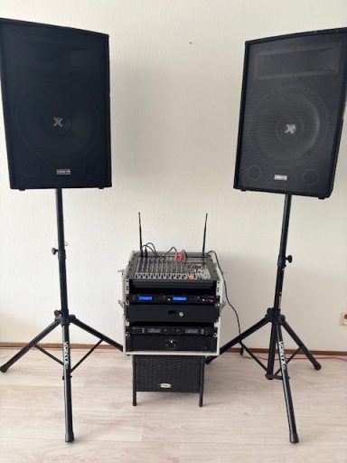 Twee zwarte luidsprekers op statieven met een audio- en mengtafel eronder.